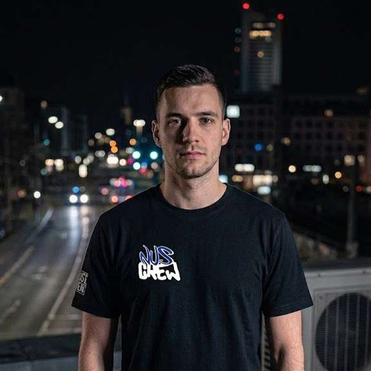 Mann trägt schwarzes T-Shirt mit Aufdruck 'eat the rich' vor nächtlicher Stadtkulisse.