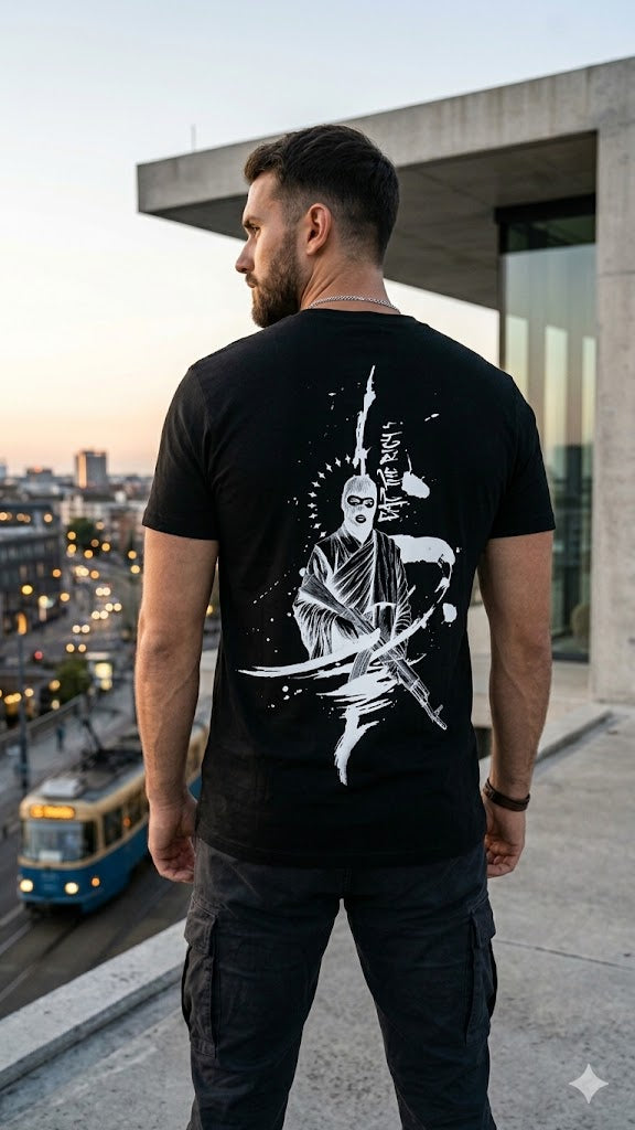 Mann von hinten in schwarzem T‑Shirt mit weißer Rückengrafik eat the rich vor urbaner Kulisse.