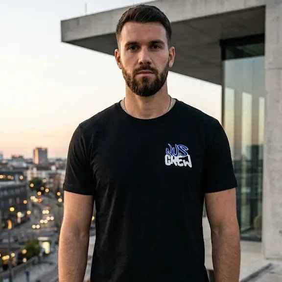 Schwarzes T-Shirt mit Print eat the rich auf der Brust, getragen von Mann vor urbanem Hintergrund.