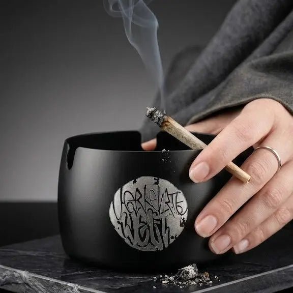 Black ashtray with artistic design, featuring a hand holding a lit cigarette.